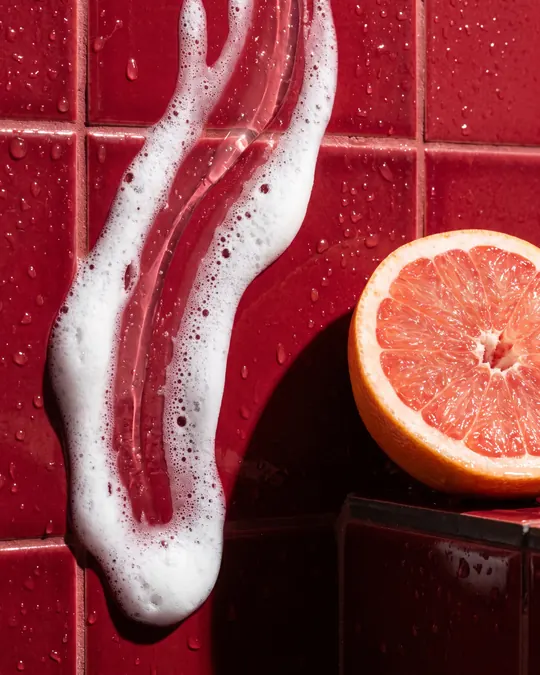 Lathered hands over red tiles beside a cut grapefruit