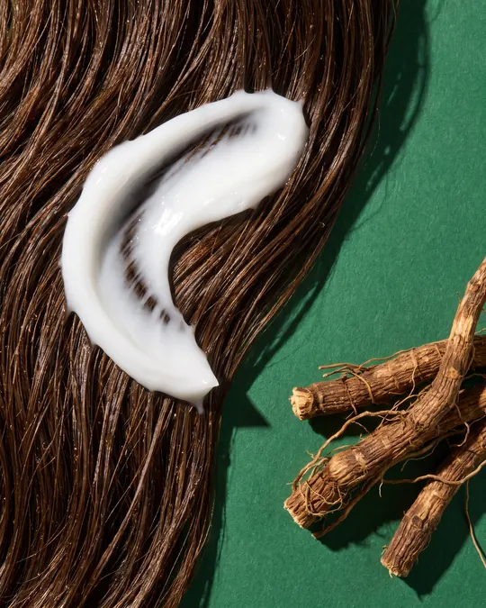 A swirl of conditioner on long dark hair, vetiver roots beside it