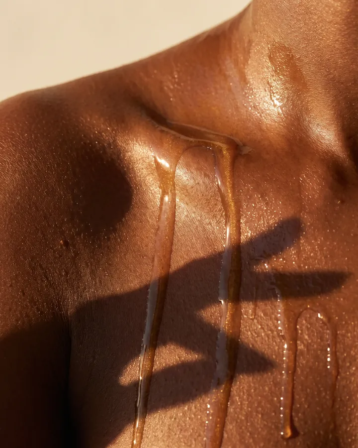 Golden oil running down glowing skin on a shoulder in low sun