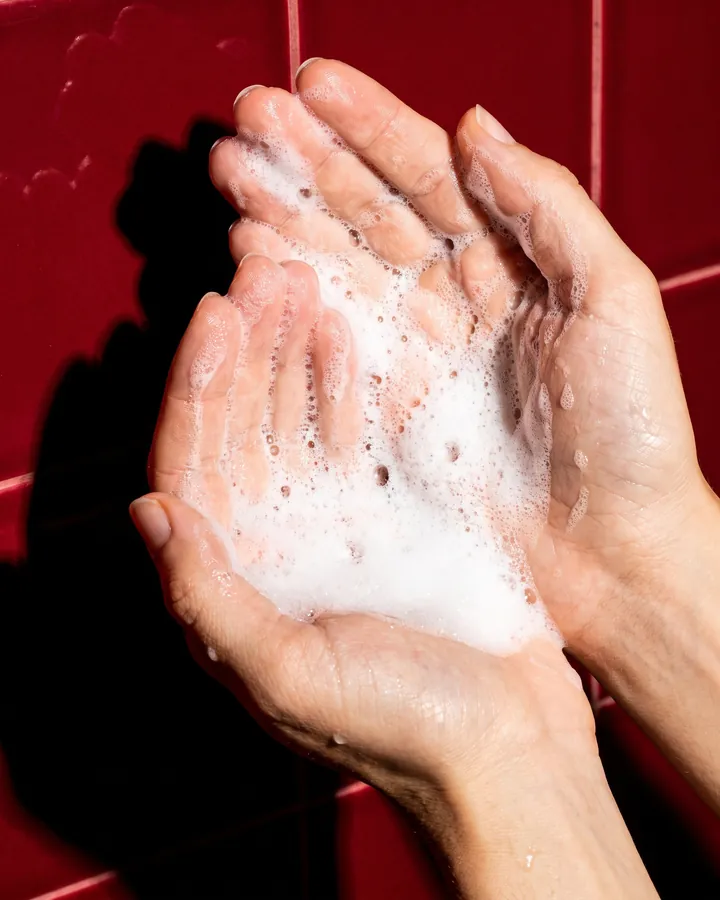 Rich white foam in two cupped hands against deep red tiles