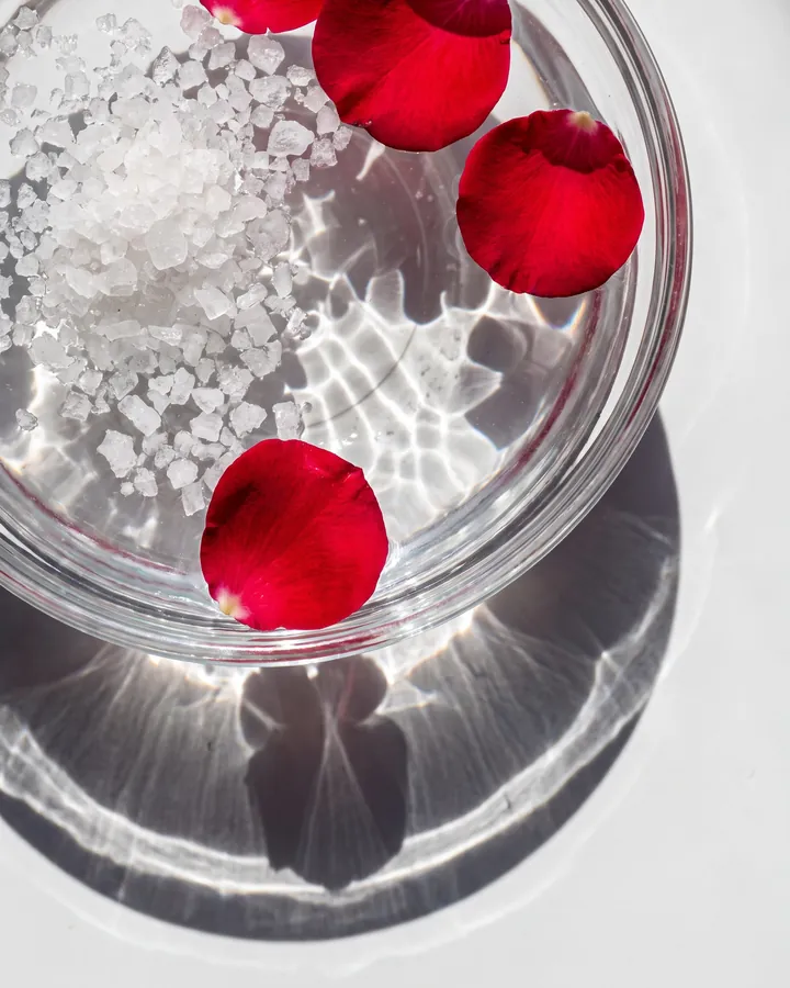 Coarse salt crystals and red petals in clear water in hard sunlight