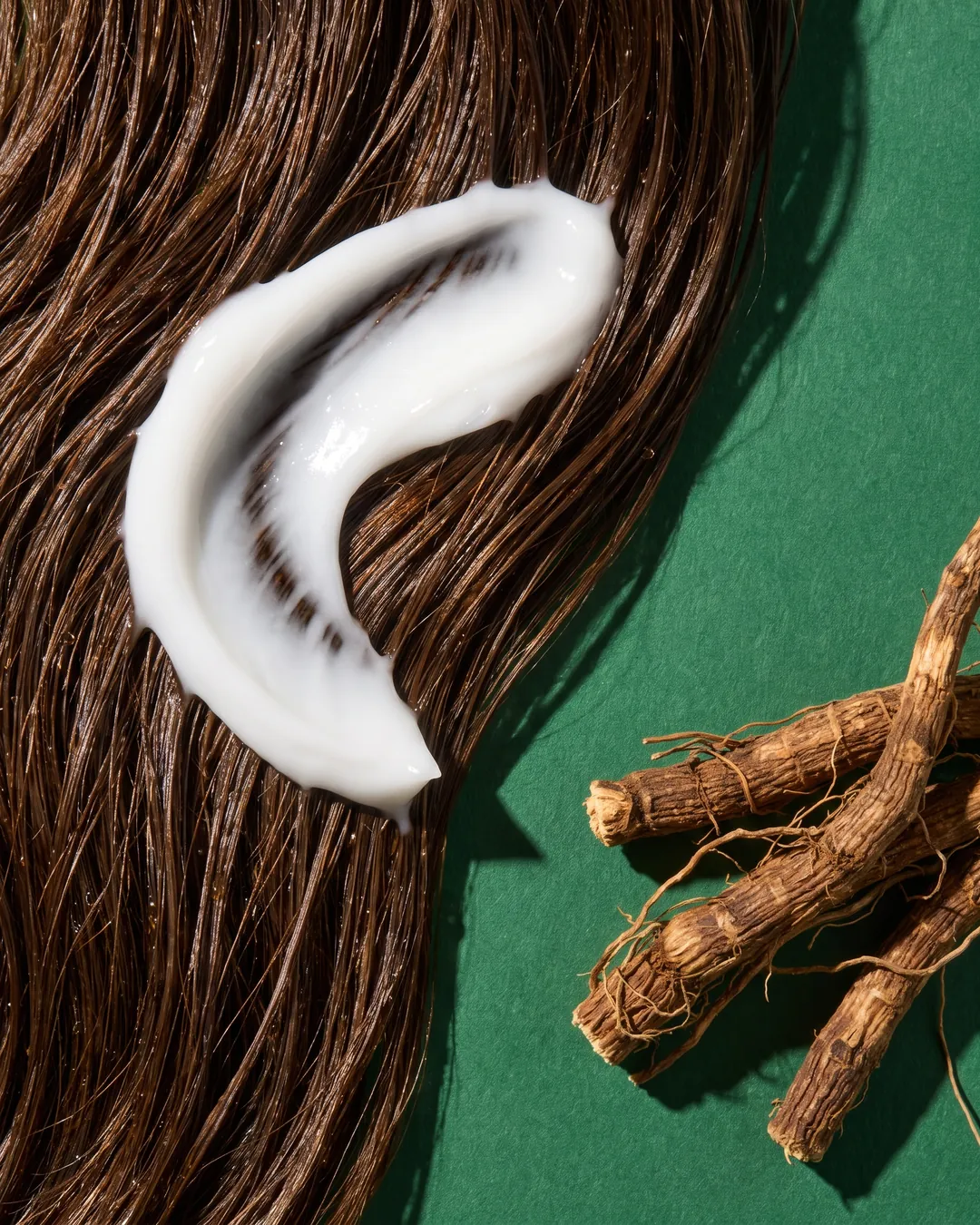 A swirl of conditioner on long dark hair, vetiver roots beside it