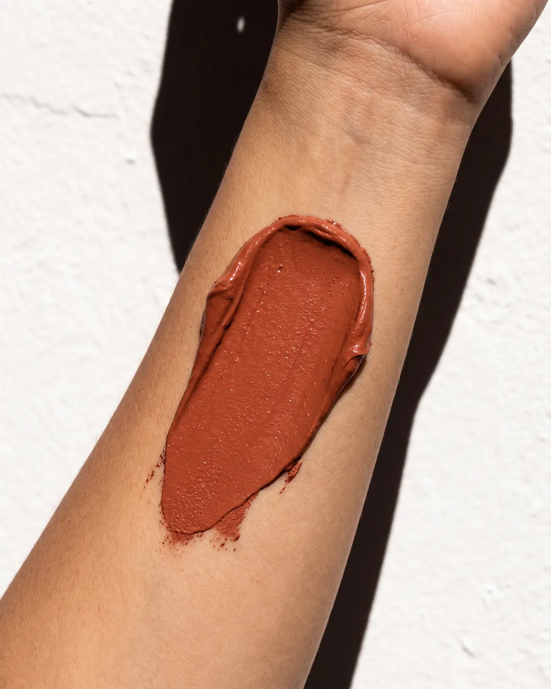 A stripe of terracotta clay on a forearm against a white wall