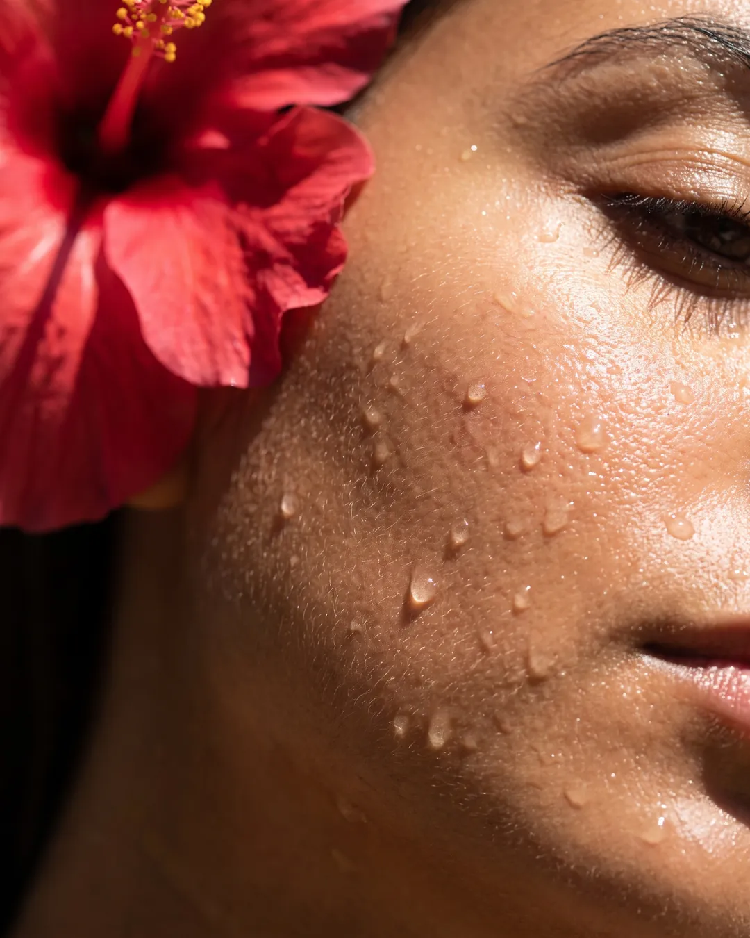 Fine drops of mist on a cheek beside a red hibiscus