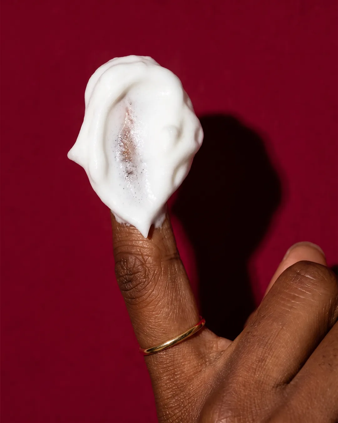 A swirl of white cream on a fingertip against a deep red wall