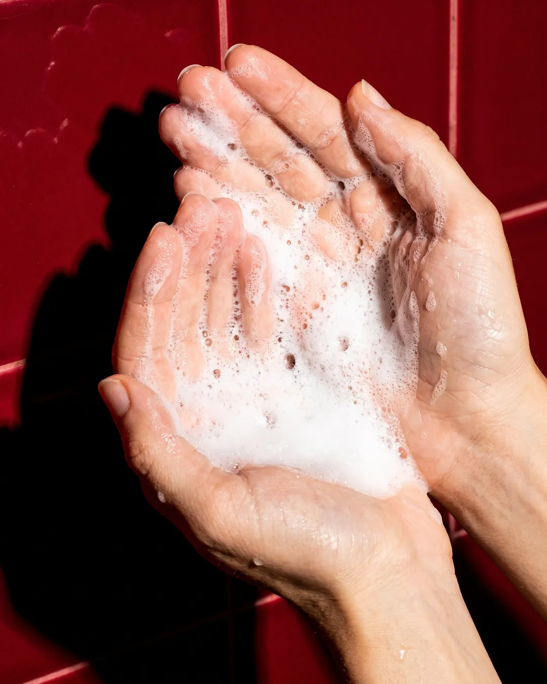 Rich white foam in two cupped hands against deep red tiles