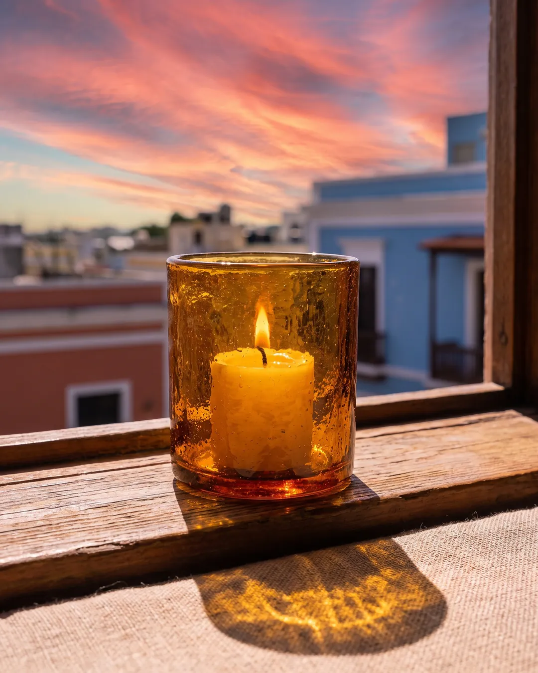 A candle burning in amber glass on a windowsill at dusk over San Juan
